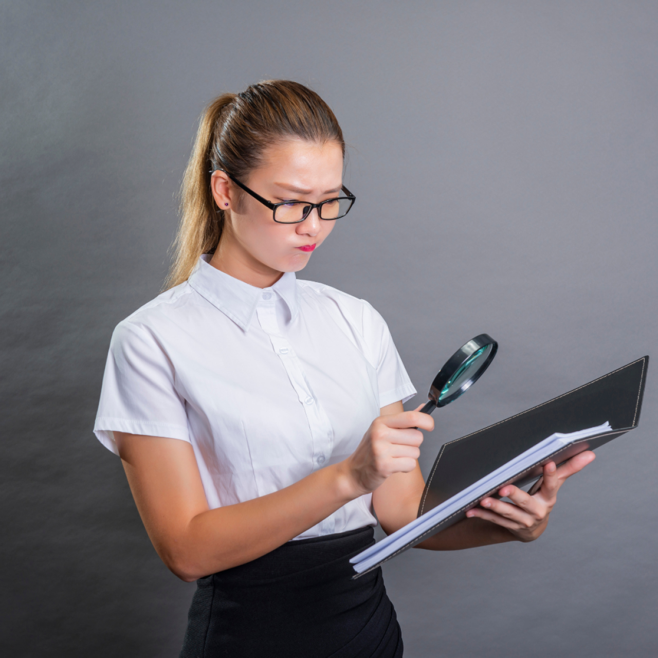 a business woman with a magnifying glass looking at some work papers.